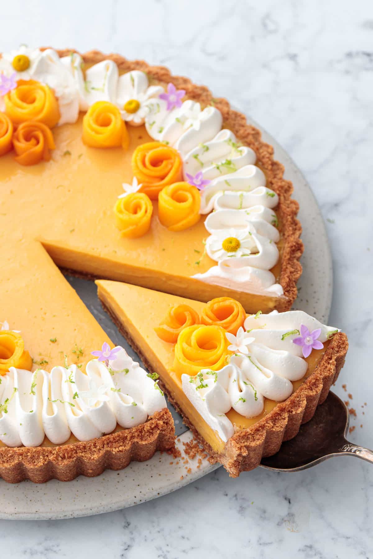 Mango Lime Tart with a slice cut out of it to show the creamy texture inside, decorated with whipped cream and edible flowers.