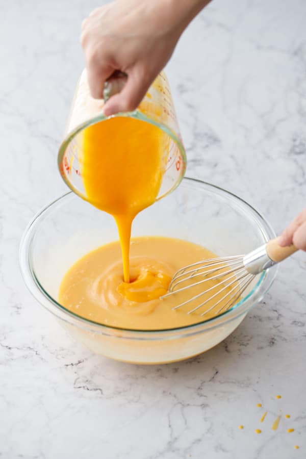 Pouring strained mango puree into the mixing bowl with the other ingredients and a whisk.