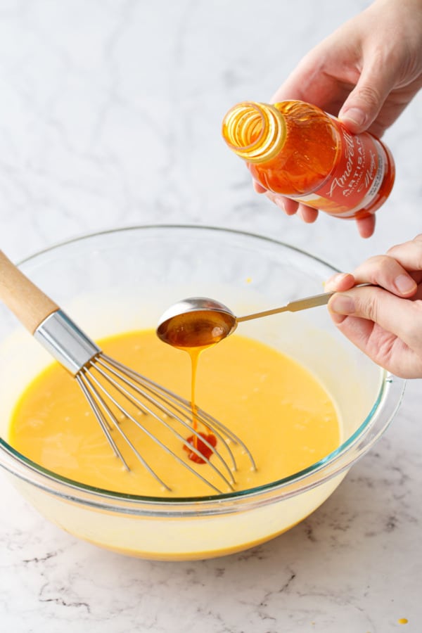 Pouring mango flavoring into the mixing bowl with the rest of the ingredients.