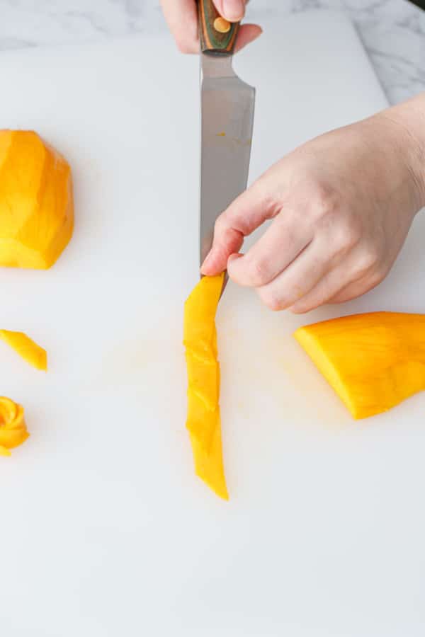 Line up thinly cut slices of mango slightly overlapping on a white cutting board.