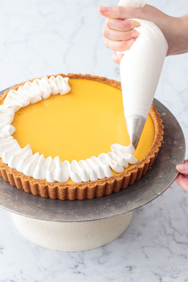 Piping squiggles of whipped cream around the border of the baked Mango Lime Tart.