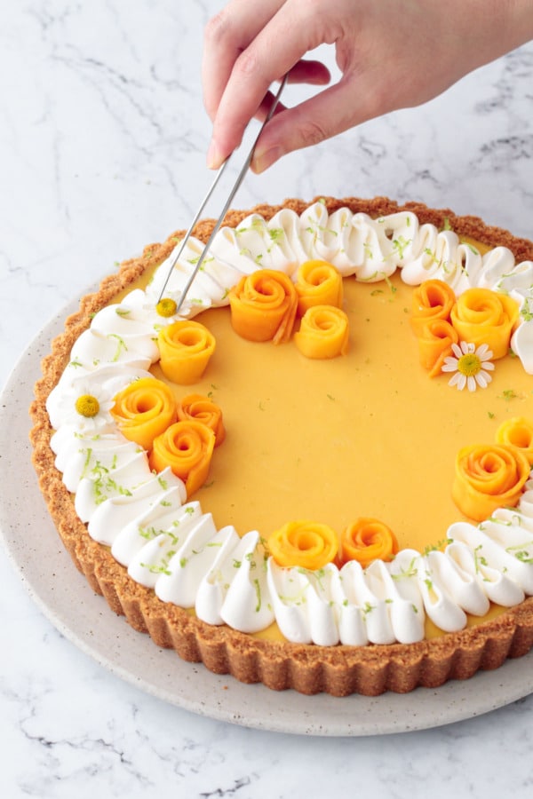 Tweezers placing edible chamomile flowers on top of the finished tart for decoration.