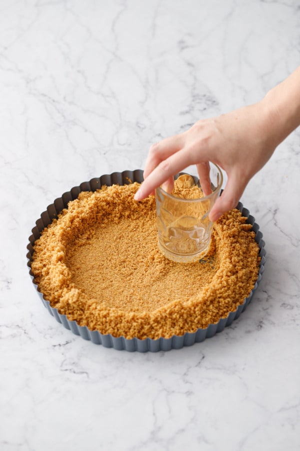 Using a juice glass to press the graham crackers into the tart pan.