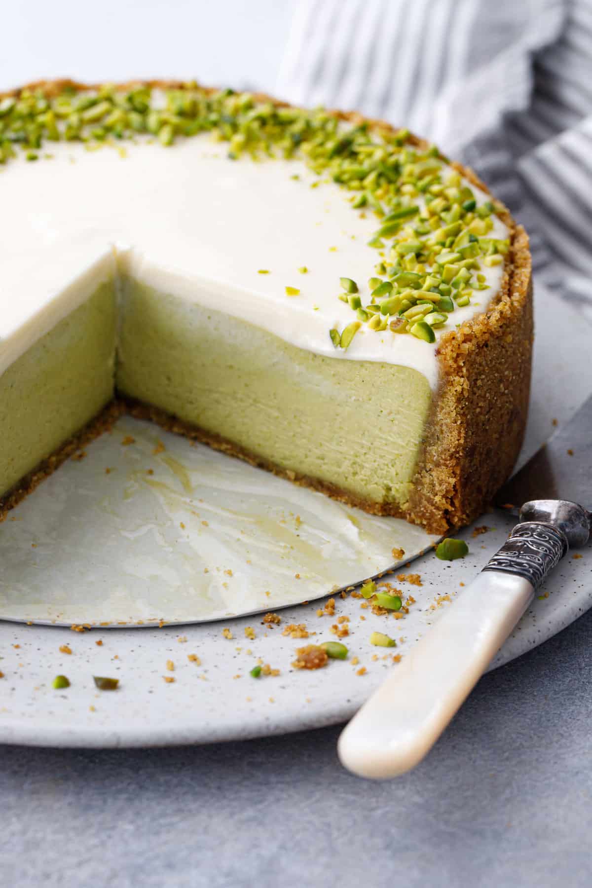 Cross section with slices cut out of a Pistachio Sour Cream Cheesecake showing the distinct layers of green pistachio filling and sour cream topping.