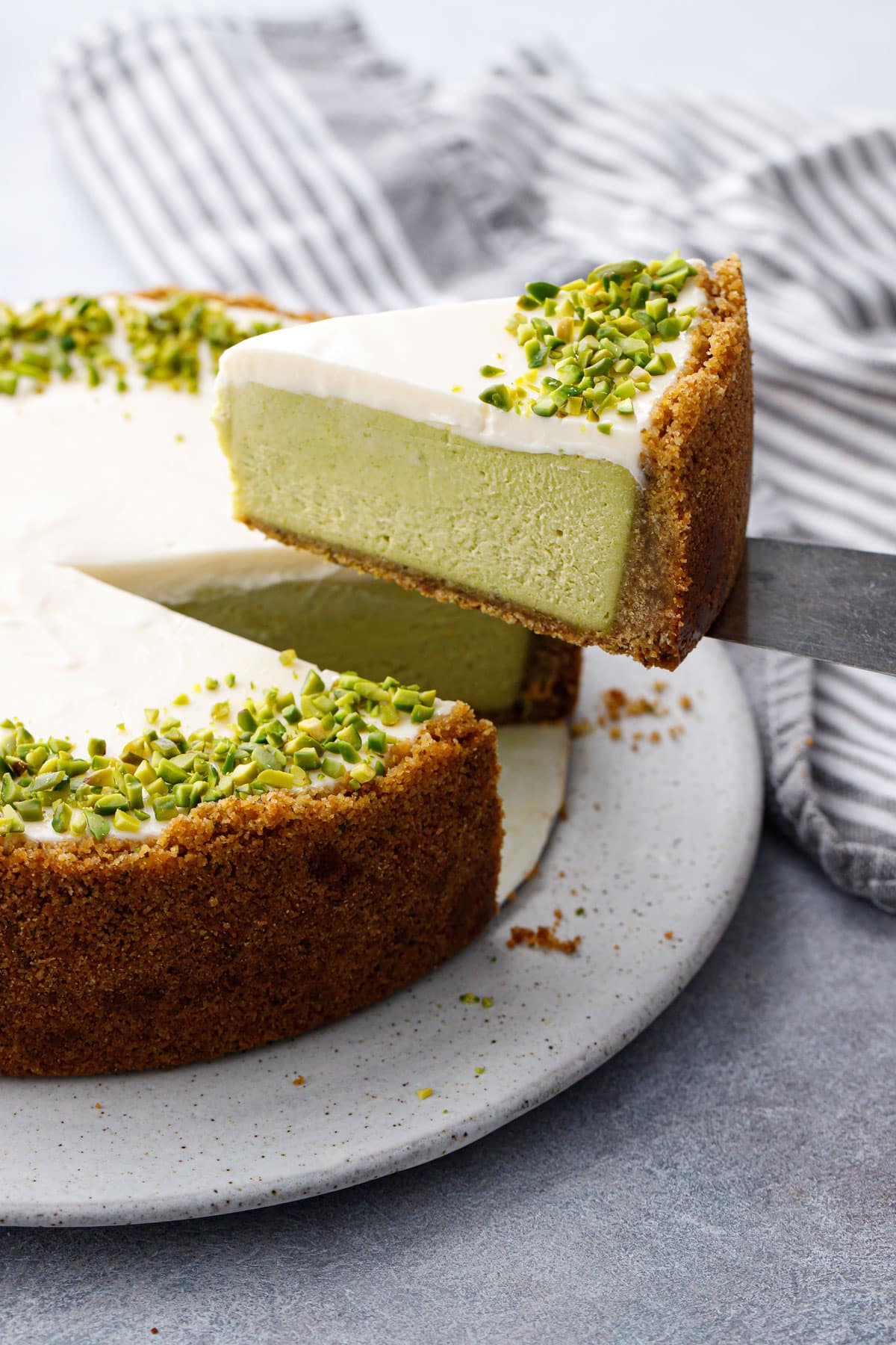 Lifting a slice of Pistachio Sour Cream Cheesecake showing the layers of green pistachio filling and sour cream topping.