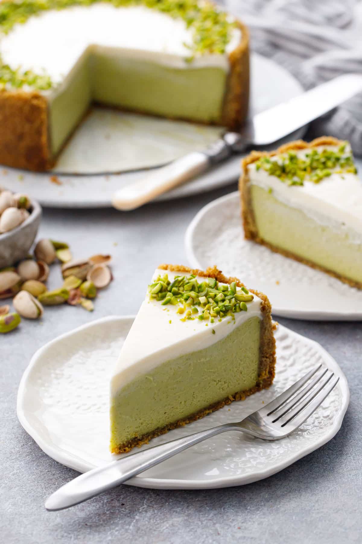 Perfectly cut slices of Pistachio Sour Cream Cheesecake with a green-tinted filling, sour cream layer, and a border of chopped green pistachios.