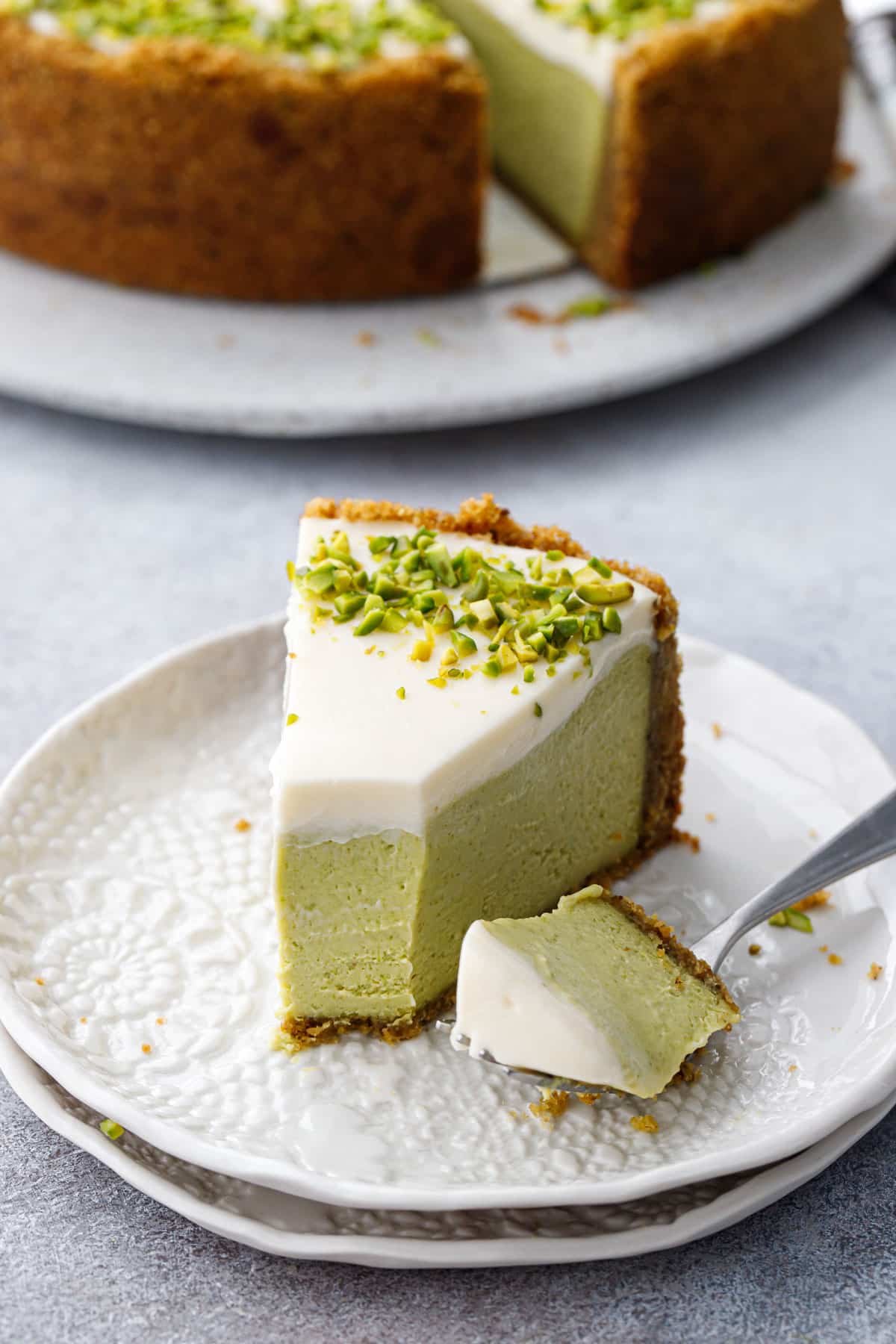 Slice of Pistachio Sour Cream Cheesecake with a bite taken out of it showing the distinct layers.