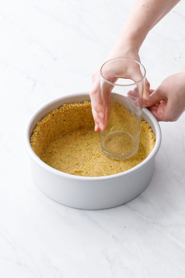 Using a tall glass to compress the crust mixture in the bottom and up the sides of the cheesecake pan.