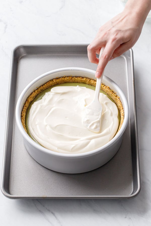 Spreading the sour cream topping in an even layer on top of the cheesecake with a spatula.