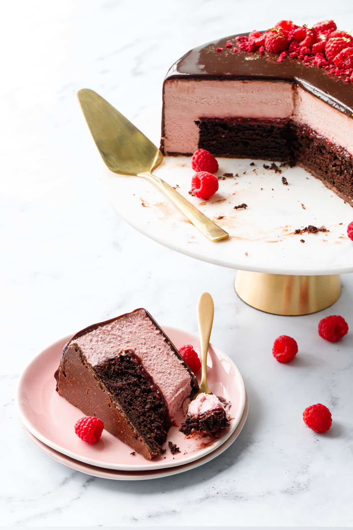 Slice of Chocolate Raspberry Mousse Cake with a bite taken out to show the fluffy texture of the raspberry mousse, on a pink plate with gold fork.