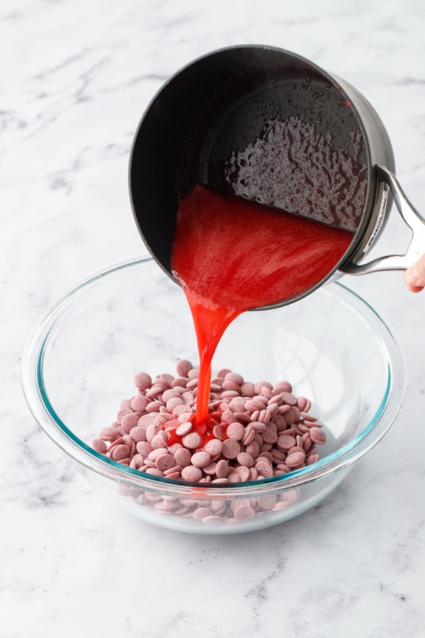 Pouring the warm raspberry puree over top of a glass bowl filled with callets of pink ruby chocolate.