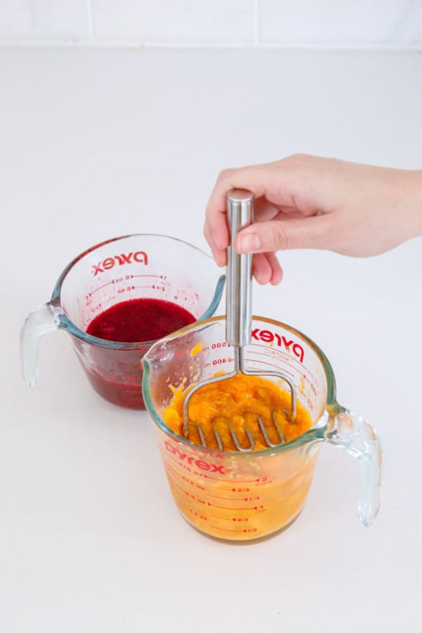 Mashing fresh mango and raspberries to prepare for jam making.