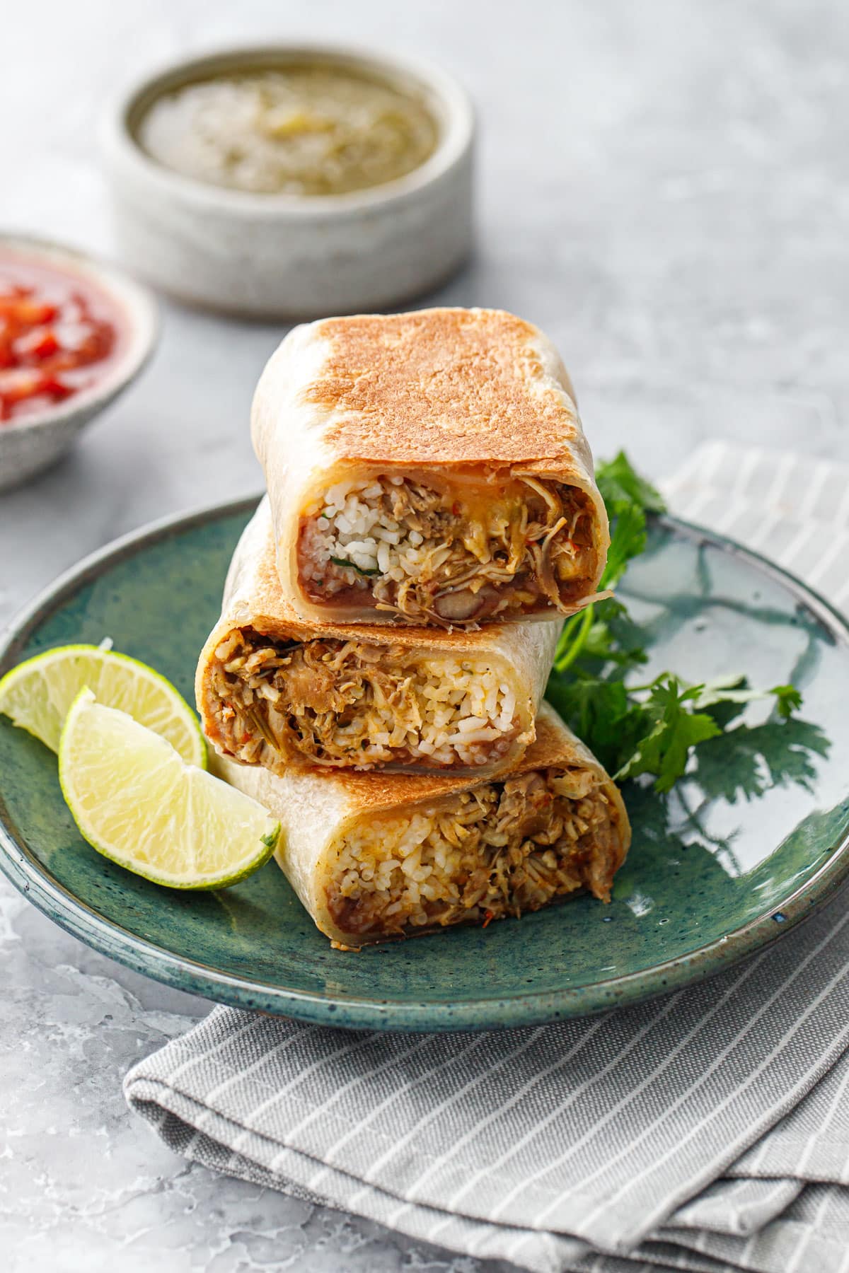 Stack of three cut halves of Crispy Chicken, Rice, & Bean Burritos on a green plate, cut to show a cross section of the filling inside.