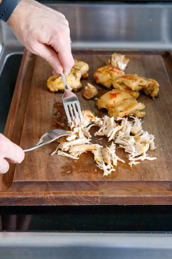 Shredding cooked chicken thighs on a wooden cutting board.