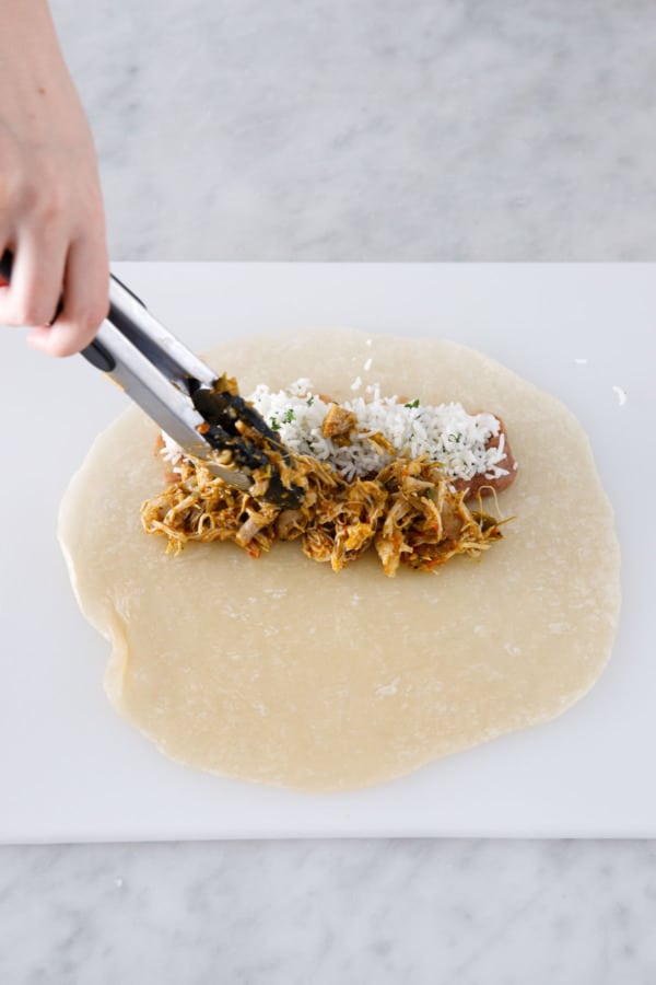 Adding refried beans, rice, and chicken filling to flour tortillas.