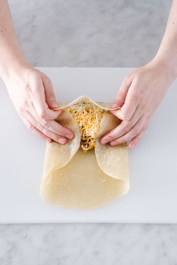 Rolling up the flour tortilla with filling inside, folding in the sides to keep the filling contained.