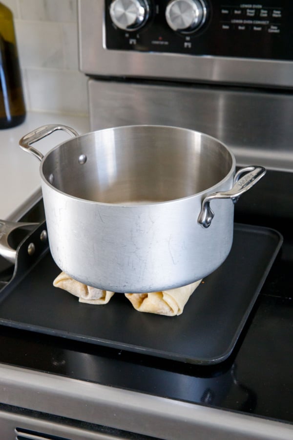 Two burritos on a flat griddle pan, with a stainless pot sitting on top to weight them down.