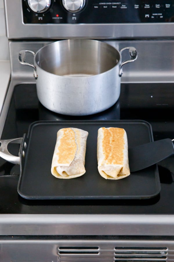 Two burritos on a flat griddle pan, golden brown on the top.