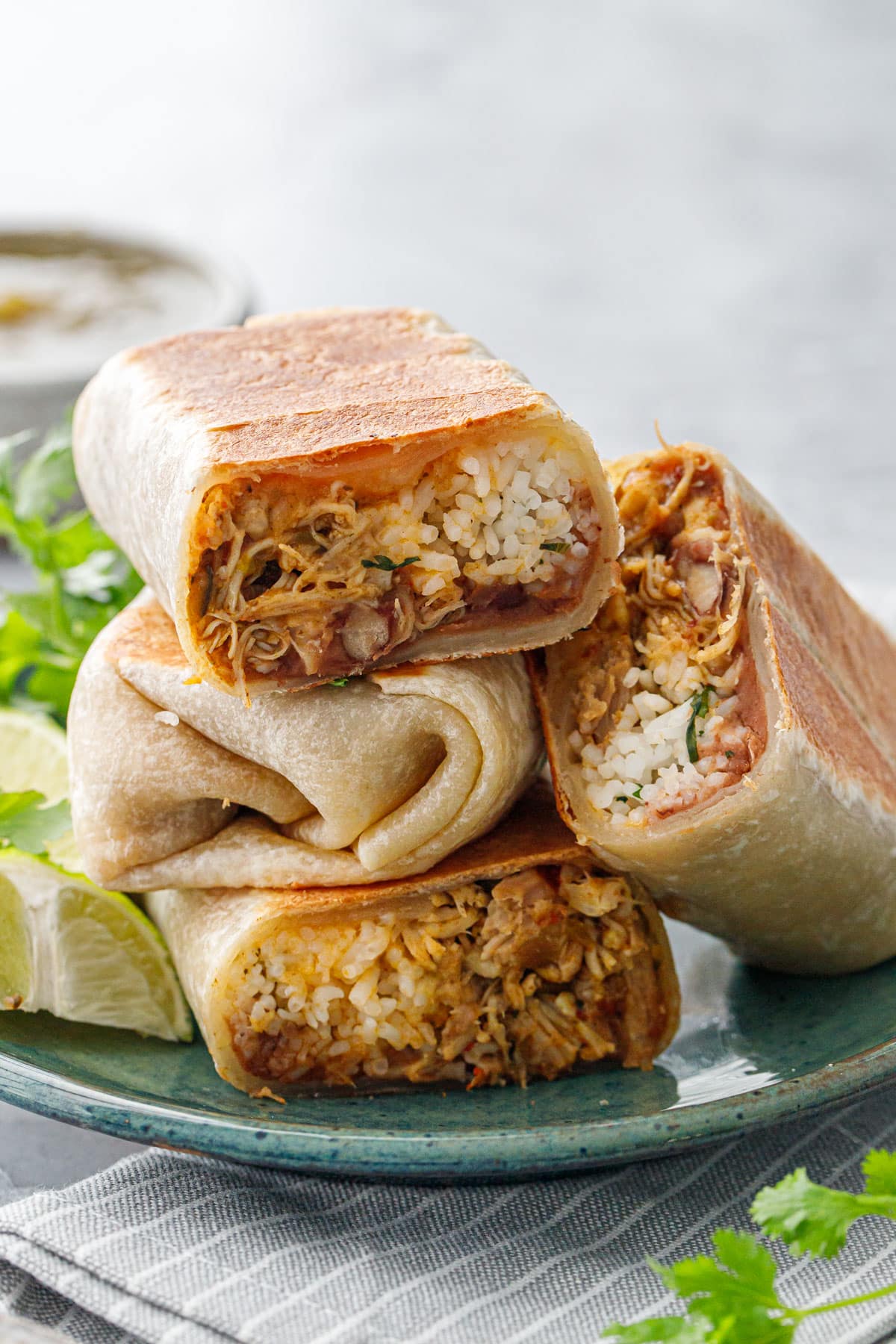 Stacked half Crispy Chicken, Rice, & Bean Burritos stacked on a plate, some facing forward to show the cross section of filling inside.