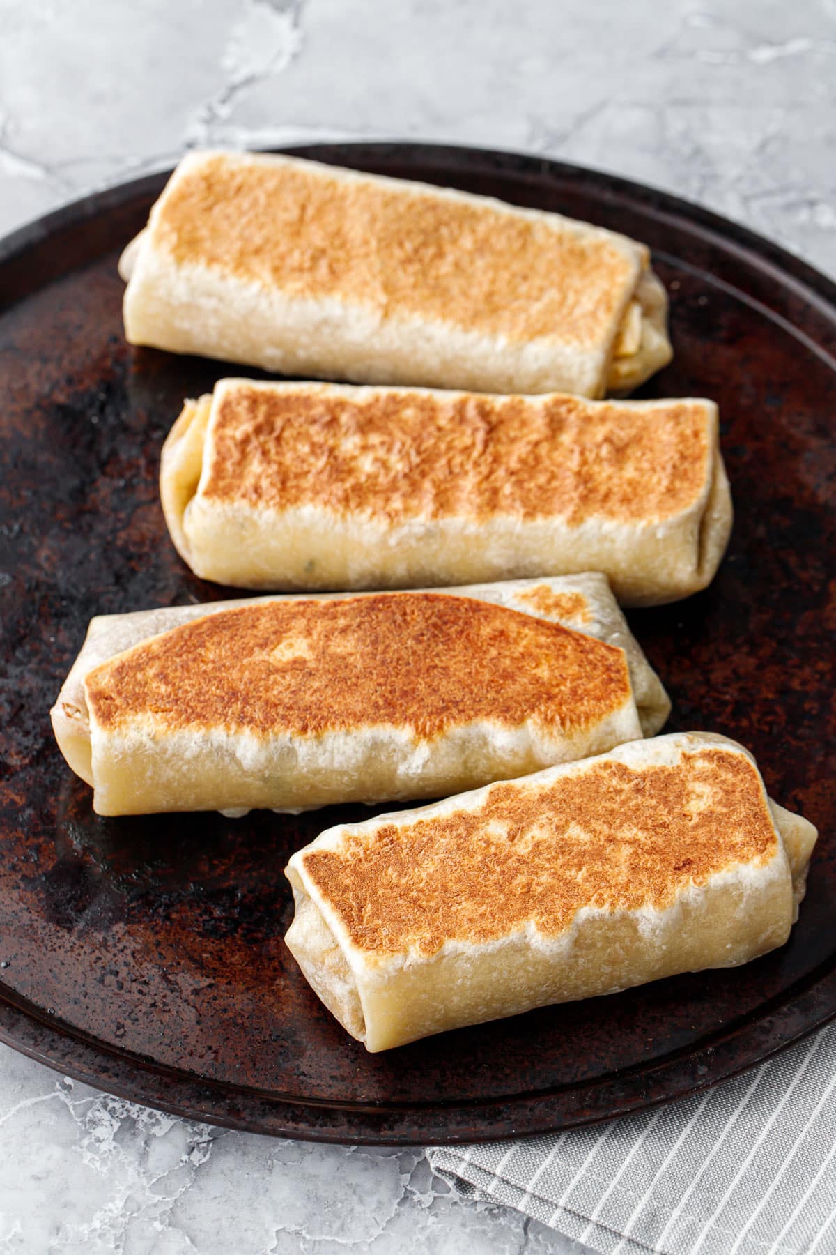 Four Crispy Chicken, Rice, & Bean Burritos on a round cookie sheet, toasted and golden brown.