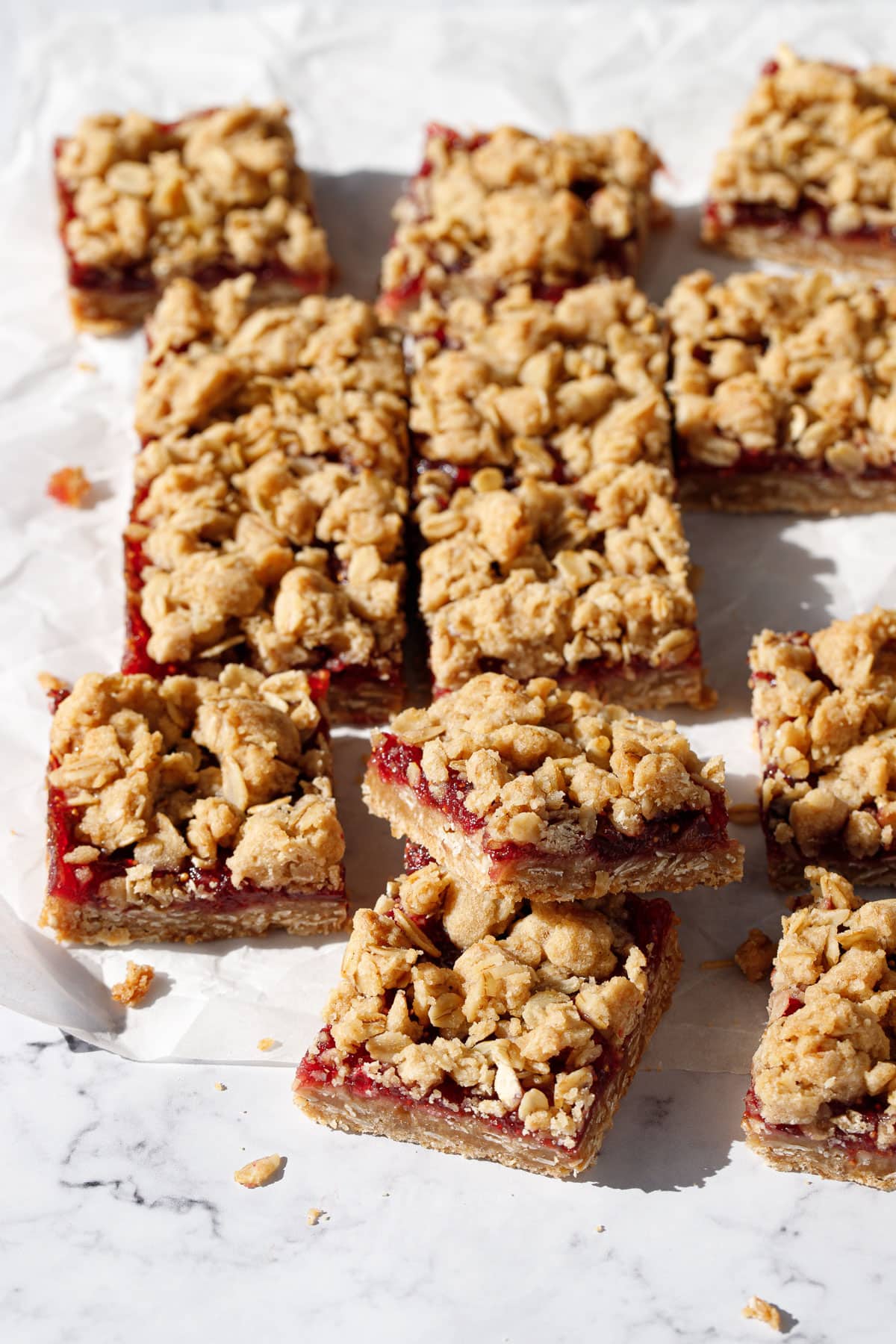 Cut squares of cookie crumb bars with a layer of purple fig jam and crumbly oat topping, on a marble background.