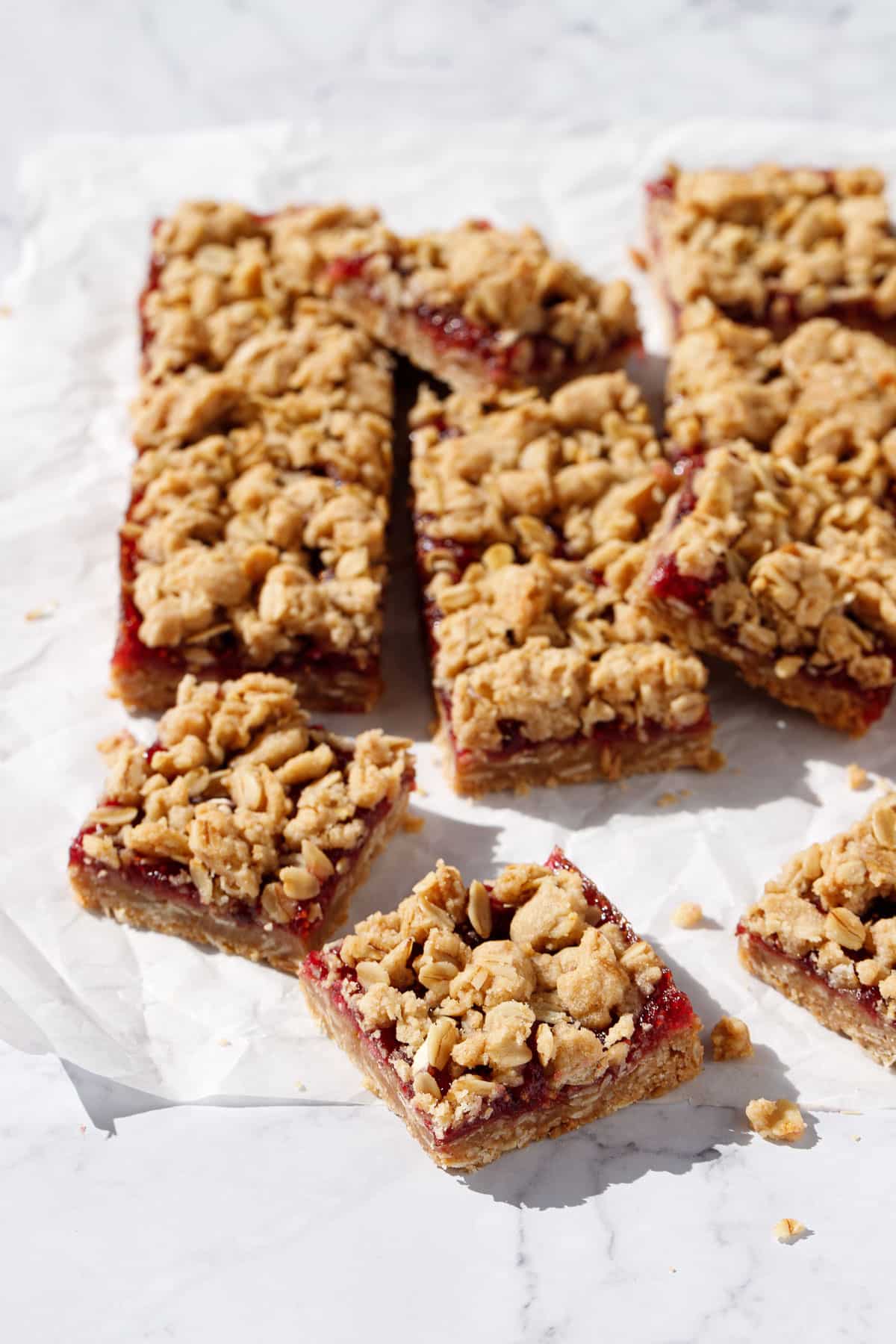 Squares of crumbly Fig, Apple & Vanilla bar cookies on a piece of crinkled parchment on a marble background.