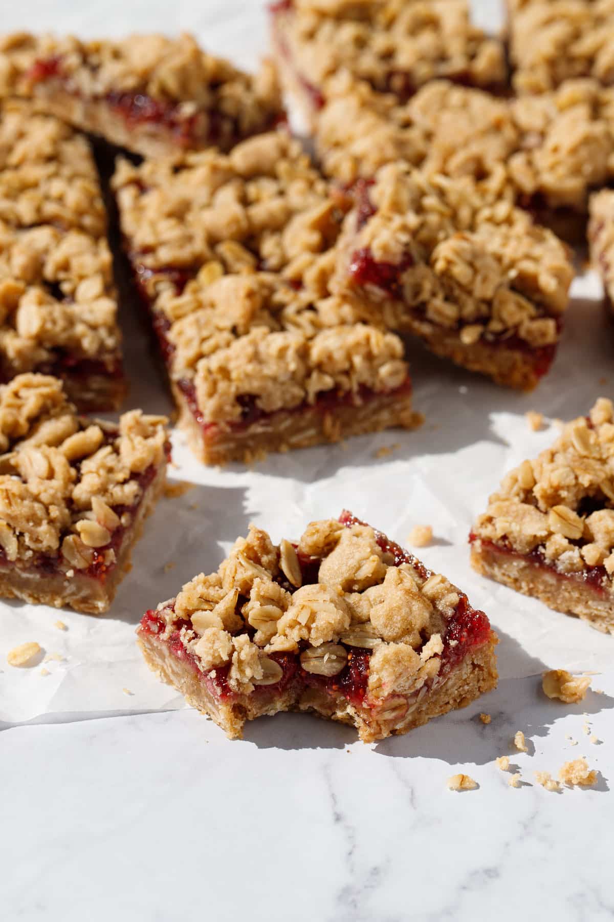 One square fig apple oat crumb bar with a bite taken out of it to show texture, more cut squares in the background.