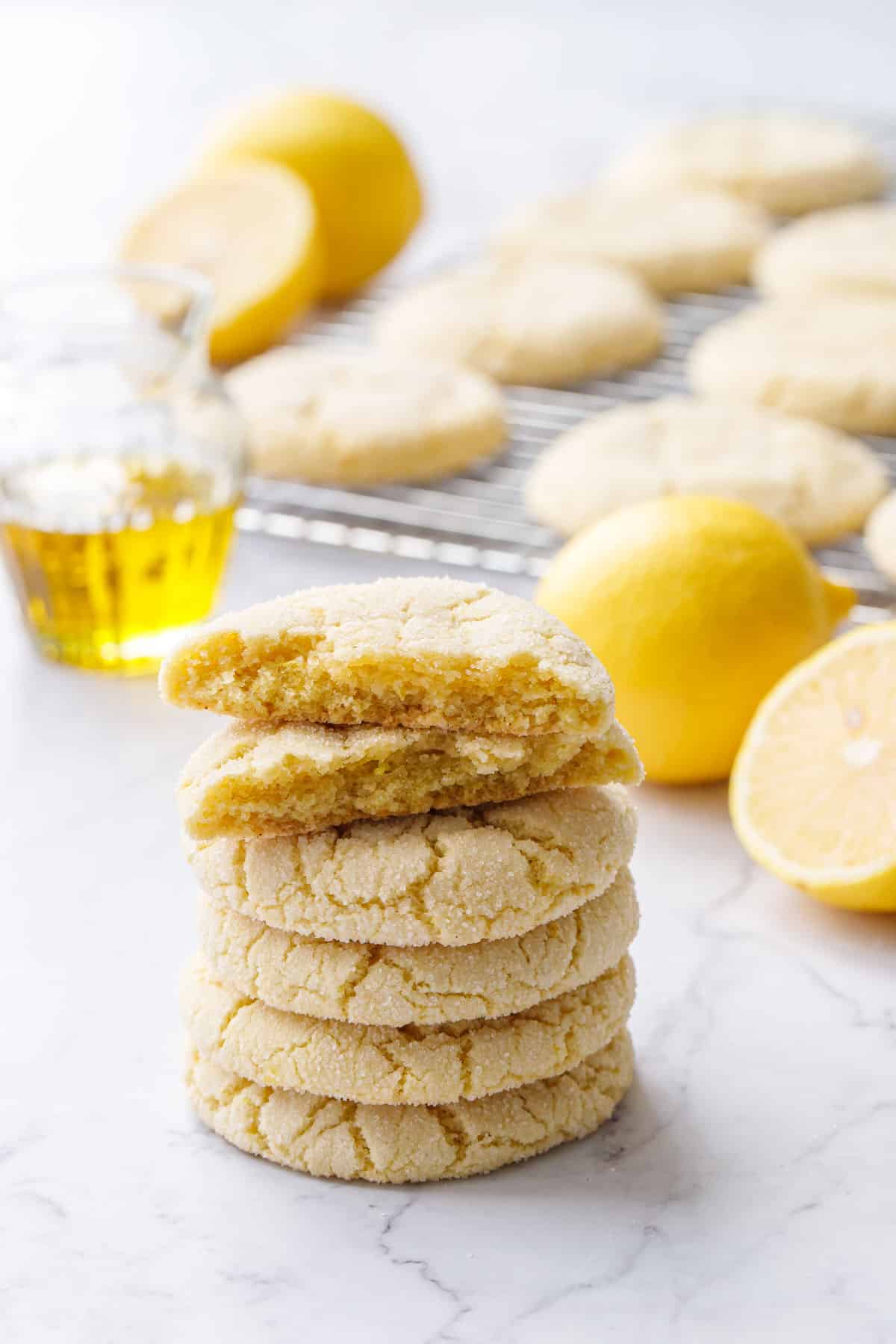 Stack of Lemon Olive Oil Sugar Cookies on a marble background, one cookie broken in half, with more in the background.