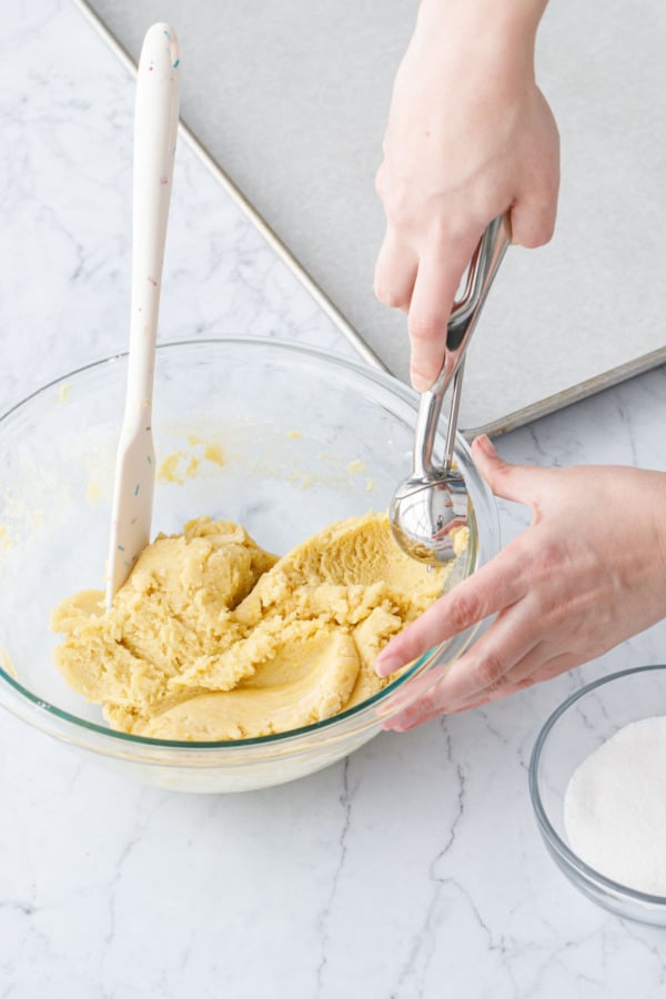 Small cookie scoop scooping some dough out of mixing bowl.