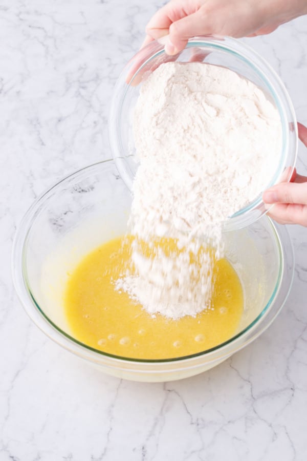 Pouring bowl of dry ingredients into mixing bowl with wet ingredients.