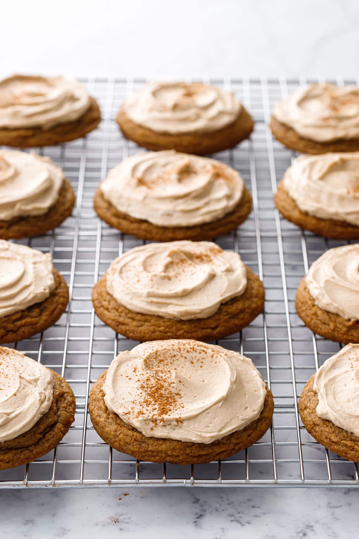 Rows of Frosted Caramel Pumpkin Cookies dusted with cinnamon on a silver wire baking rack.