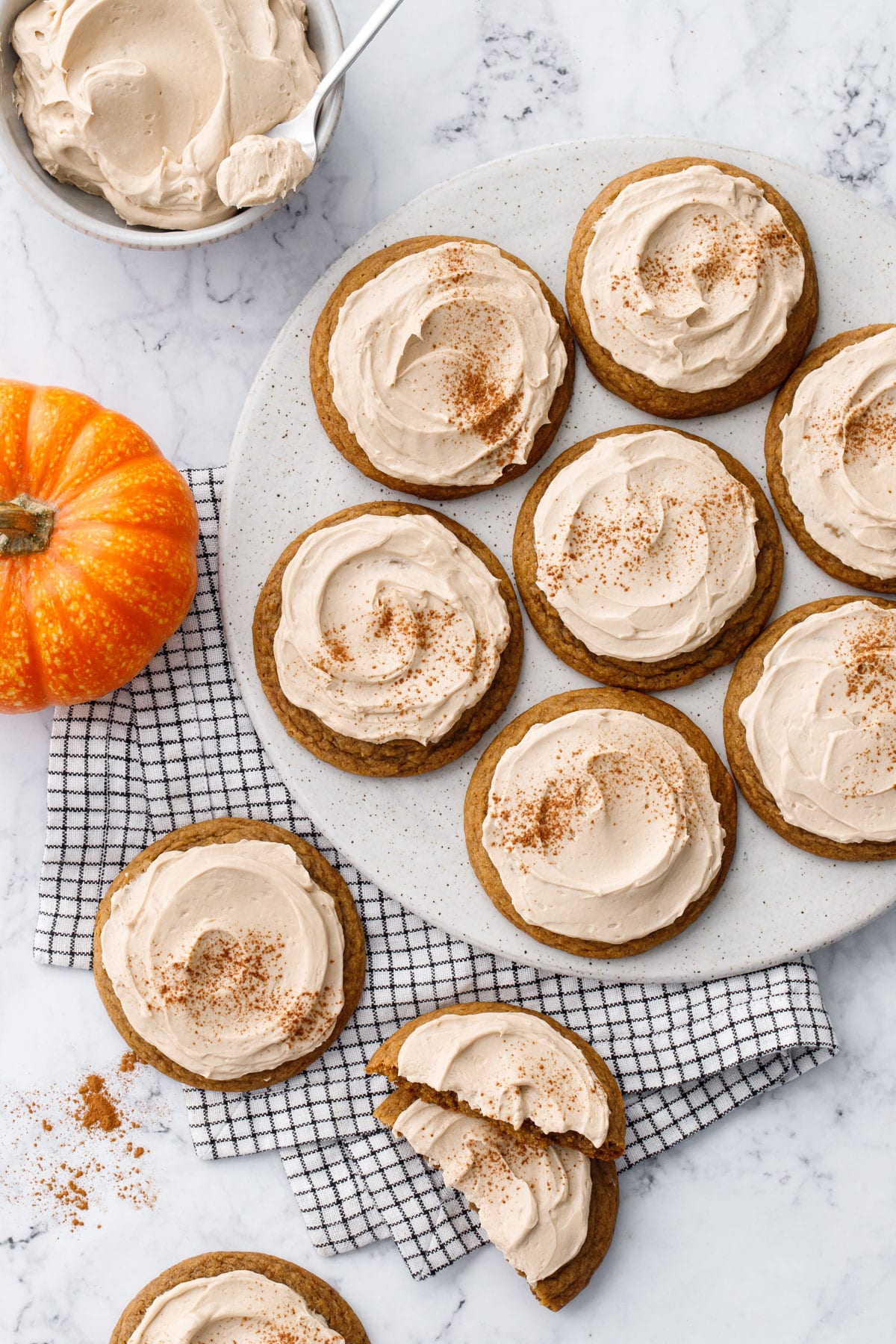 Overhead, plate with Caramel Pumpkin Cookies, plus bowl of Salted Caramel Buttercream and one small pumpkin on a striped napkin on the side.