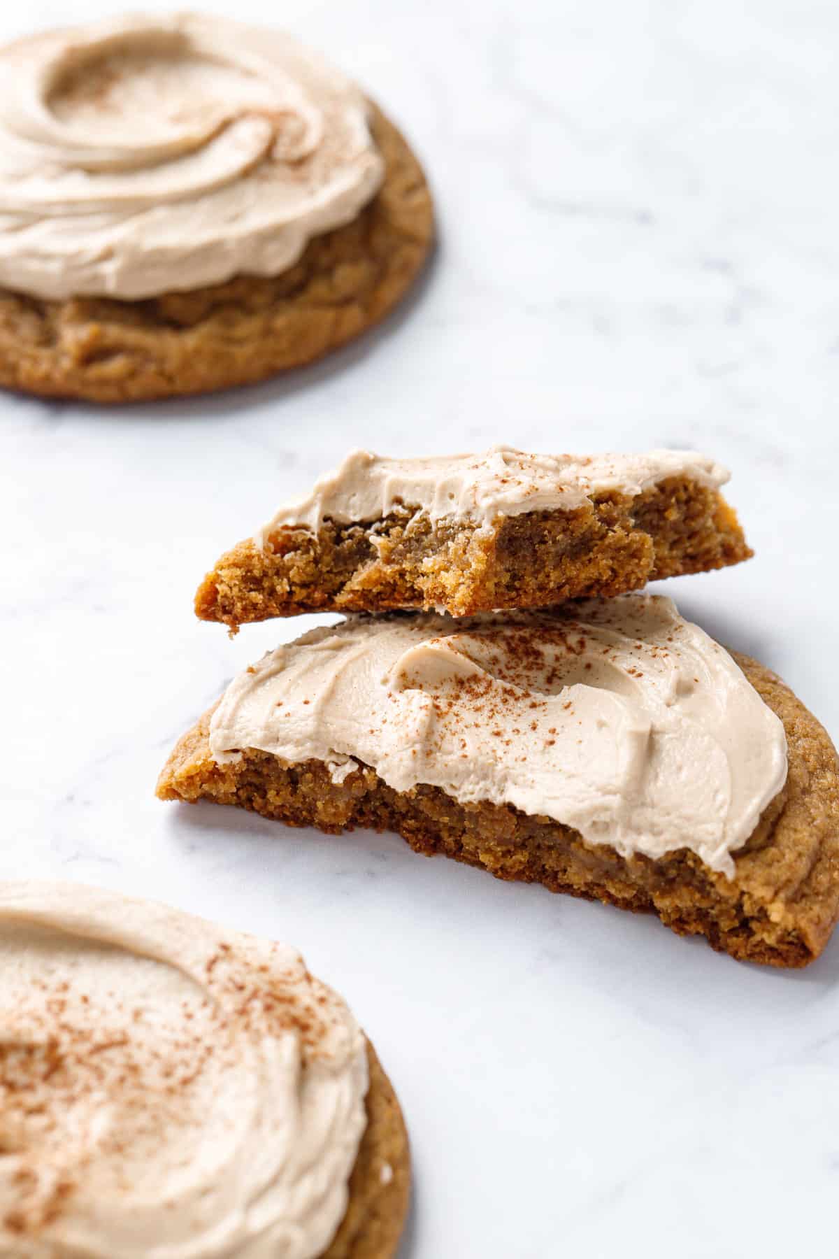 Closeup of a Frosted Caramel Pumpkin Cookie broken in half with a bite out of it to show the chewy interior texture.