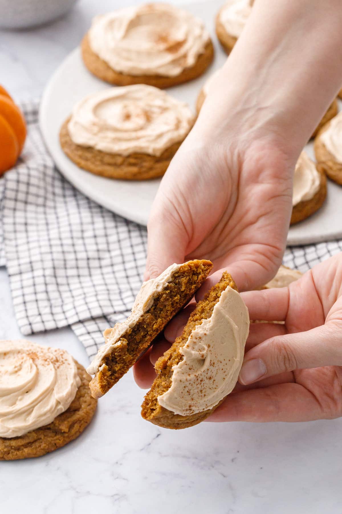 Hands breaking a Caramel Pumpkin Cookie in half to show the soft and chewy texture inside.