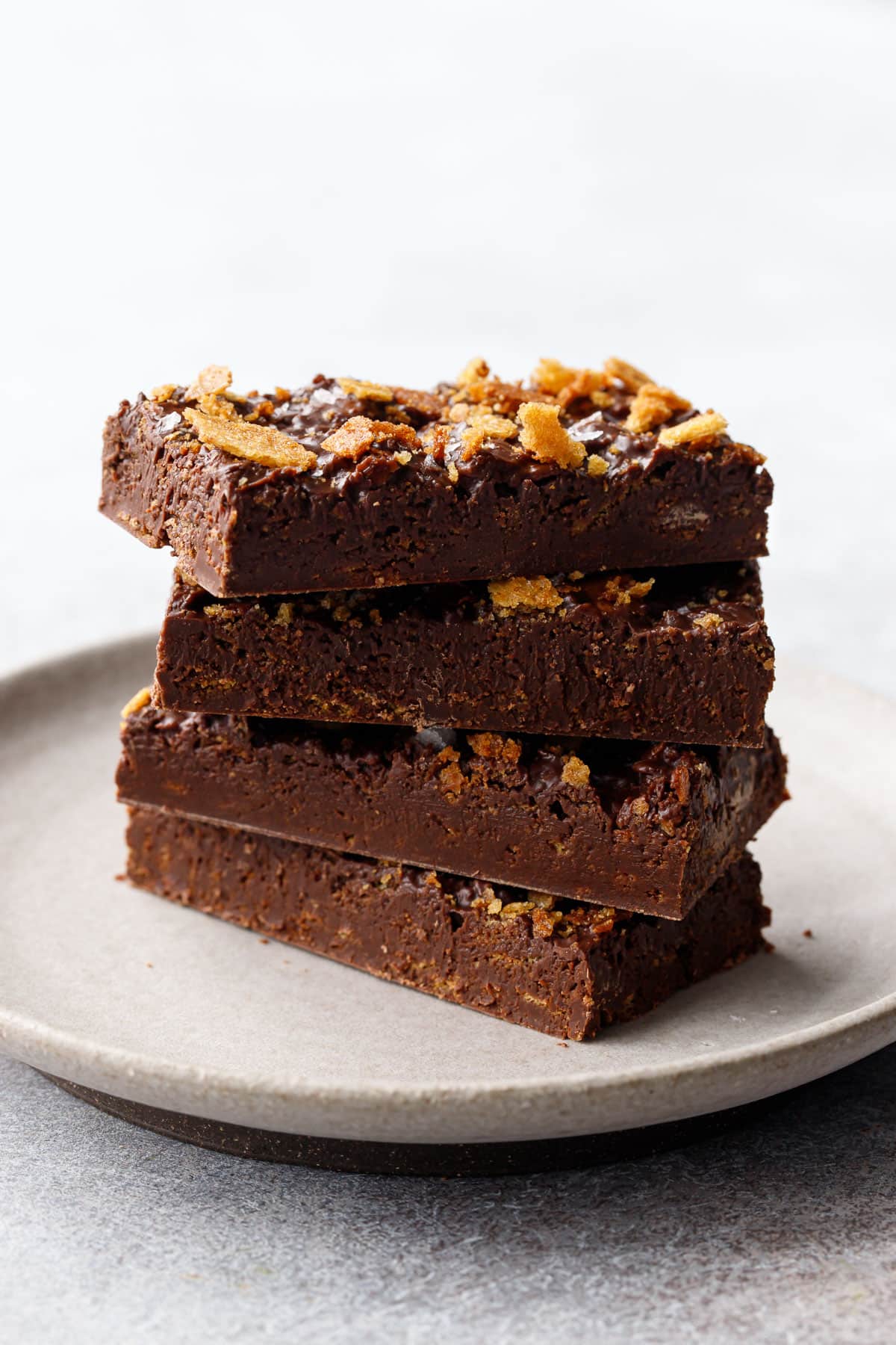 Stack of rectangular bars of Nutella Chocolate Crunch Candy Bark on a white ceramic plate on a gray textured background.