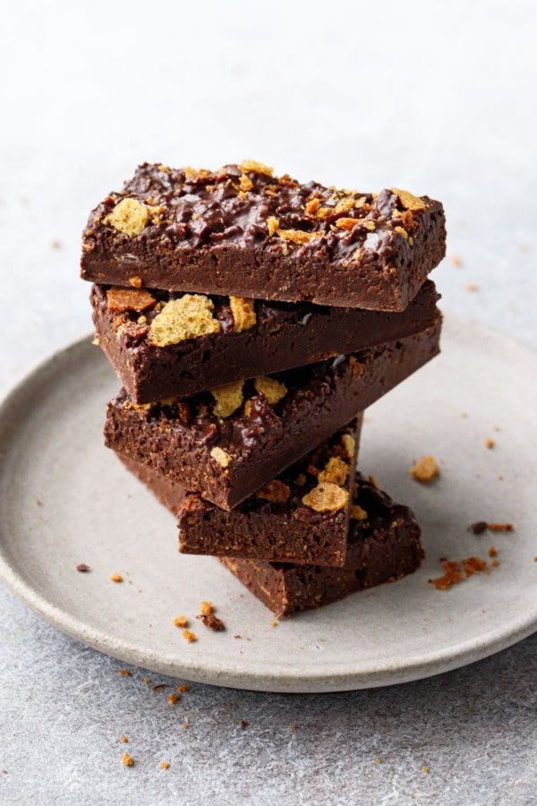 Spiraling stack of rectangular bars of Nutella Chocolate Crunch Candy Bark on a white ceramic plate, a few crumbs scattered about.