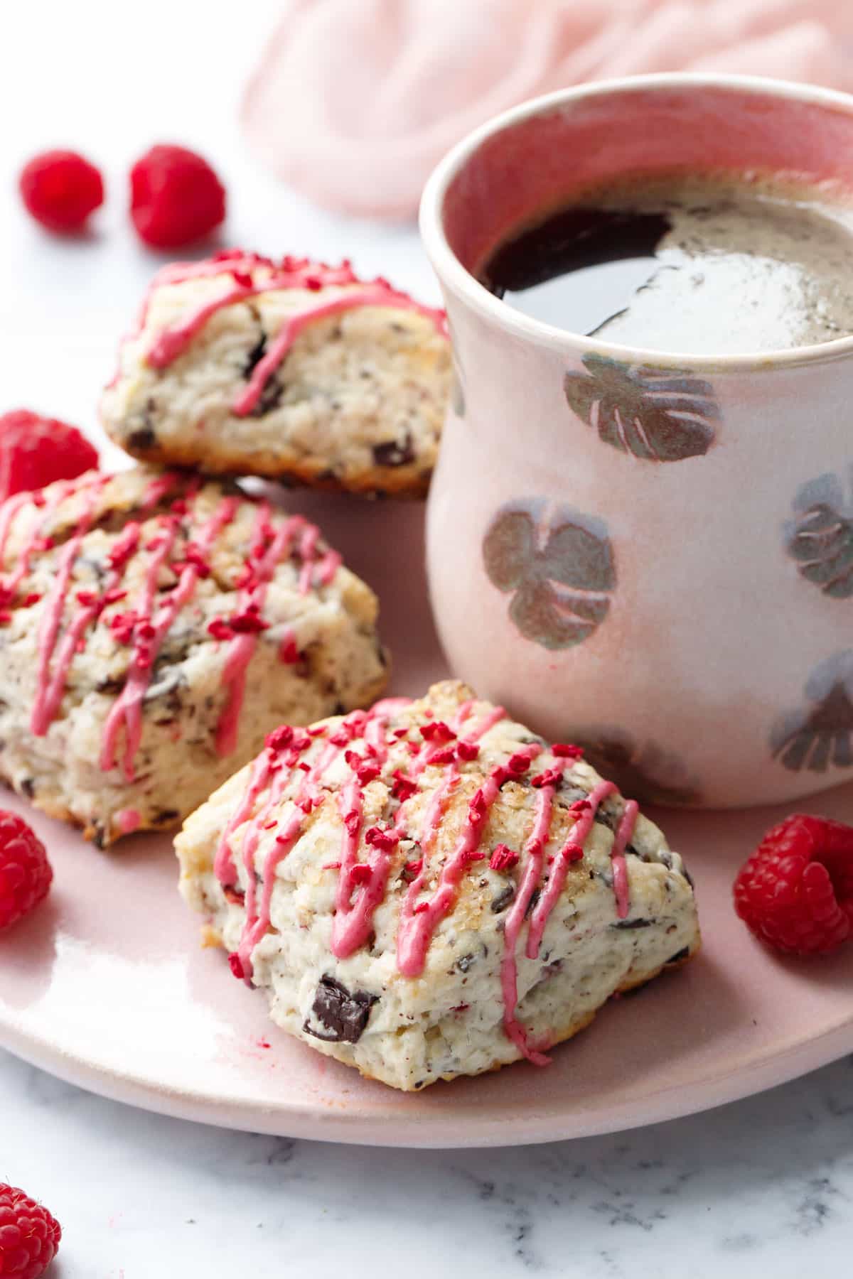 Dark Chocolate Raspberry Cream Scones on a serving plate with a ceramic mug of coffee and a few fresh raspberries.
