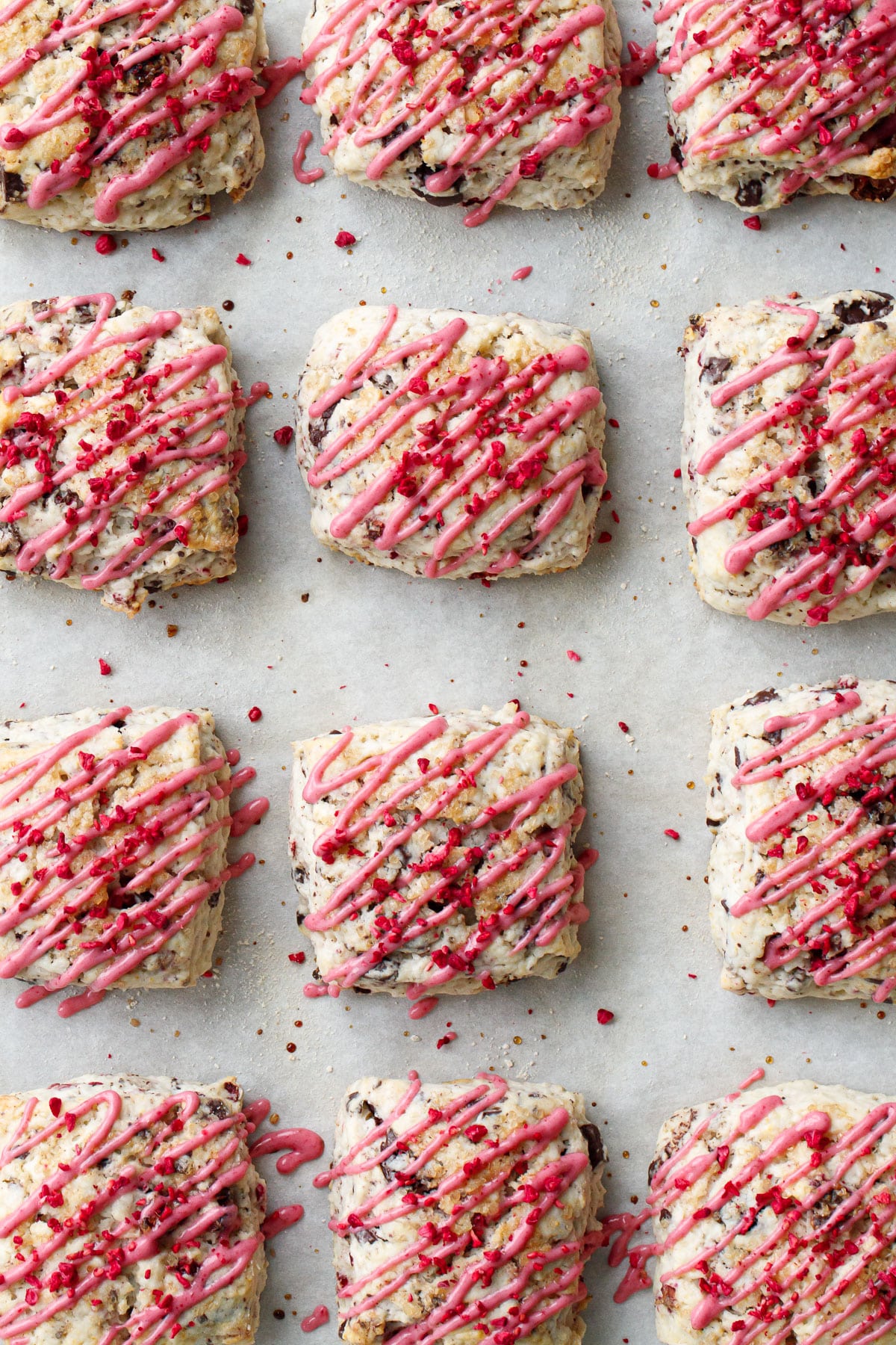 Overhead, rows of Dark Chocolate Raspberry Cream Scones drizzled with pink raspberry glaze.