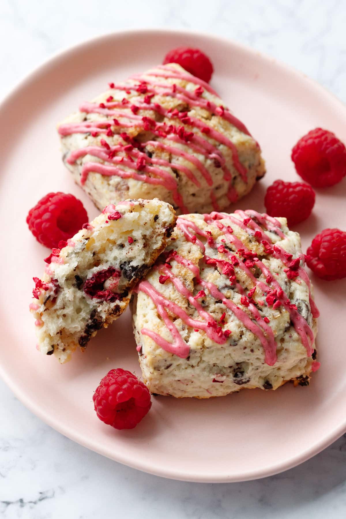 Pink plate with Dark Chocolate Raspberry Cream Scones, one broken in half to show the fluffy inner texture.