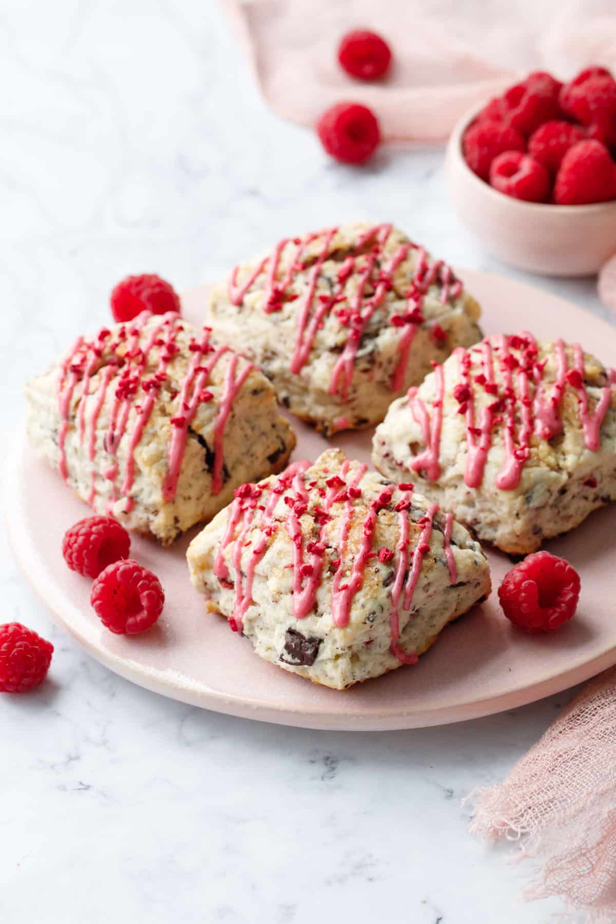 Four square Dark Chocolate Raspberry Cream Scones on a pink serving plate, with pink napkin and bowl of fresh raspberries in the background.