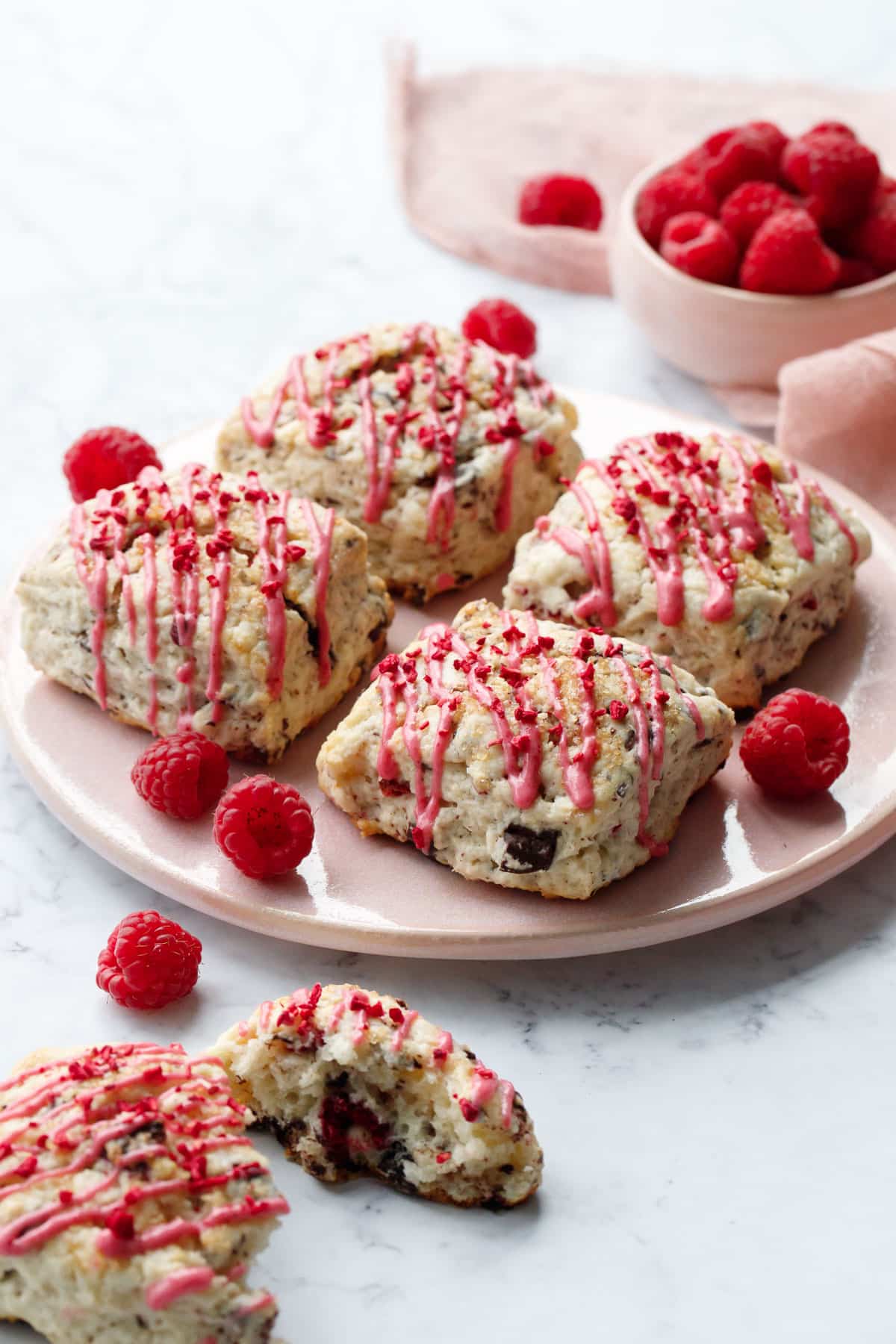 Dark Chocolate Raspberry Cream Scones on a pink plate, with one broken scone in the foreground and a bowl of fresh raspberries in the background.