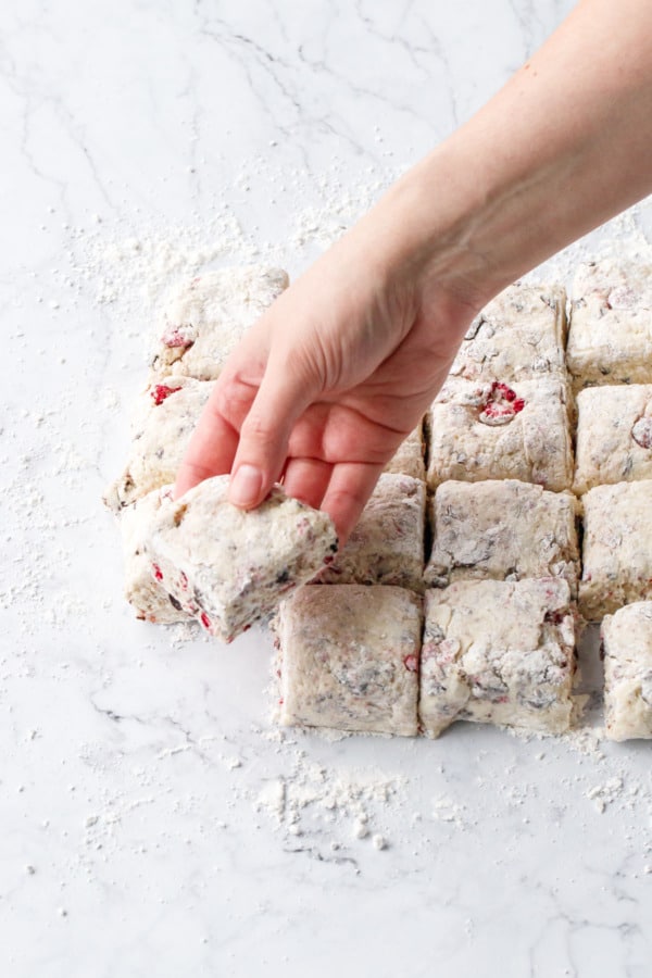 Lifting one square of unbaked scone dough off of the floured marble surface.