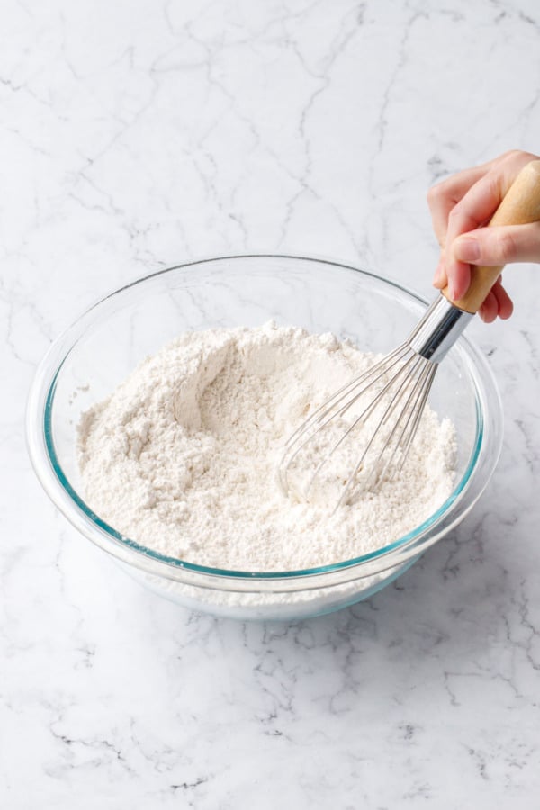 Whisking dry ingredients in a glass mixing bowl until evenly incorporated.