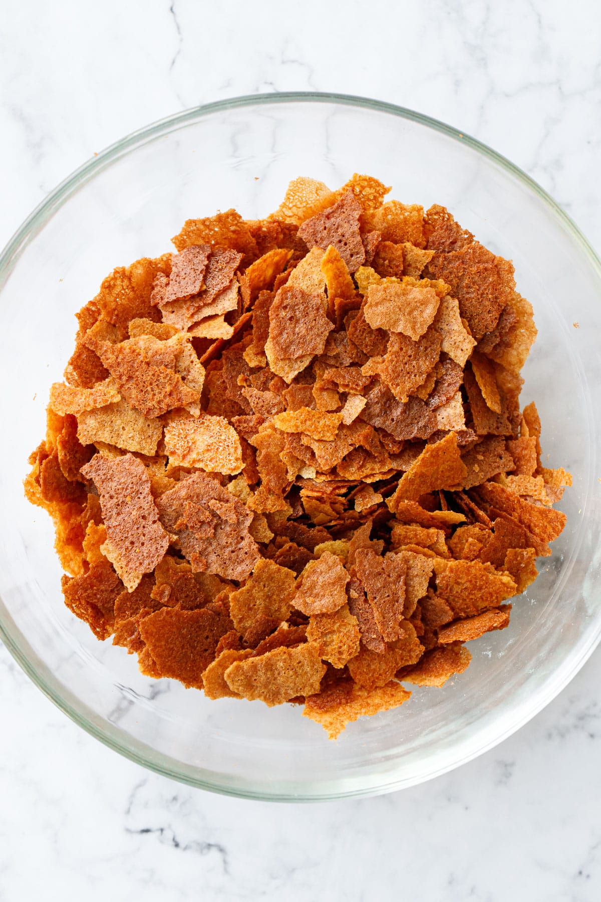 Top down view of a glass bowl filled with Homemade Feuilletine flakes on a marble background.