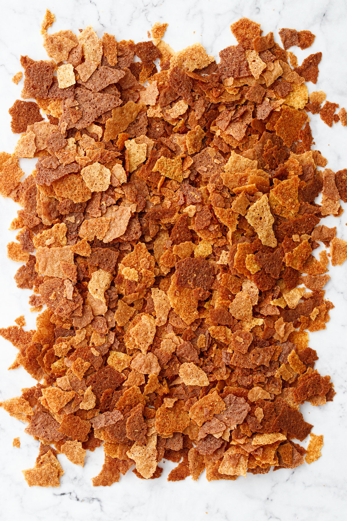 Overhead pile of golden brown flakes of homemade on a marble surface.