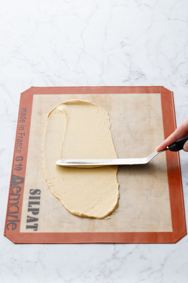 Offset spatula spreading out a thin layer of batter on a silicone baking mat.