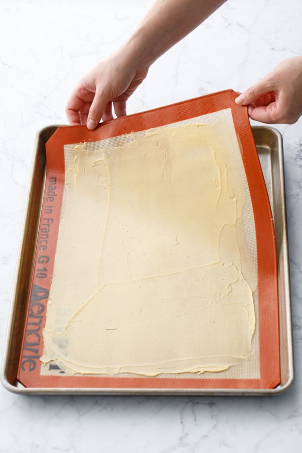 Lowering the batter-covered silicone mat into a half sheet pan before baking.