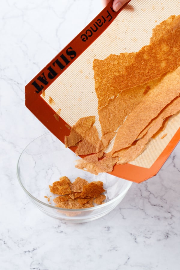 Folding the silicone mat and pouring the broken up feuilletine flakes into a glass bowl.