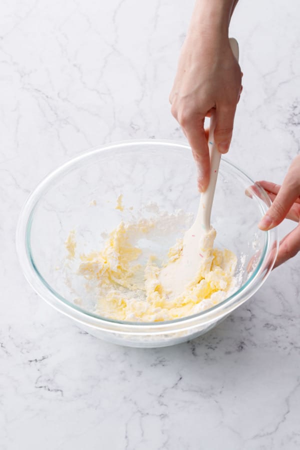 Using a silicone spatula to smush the powdered sugar and butter together.