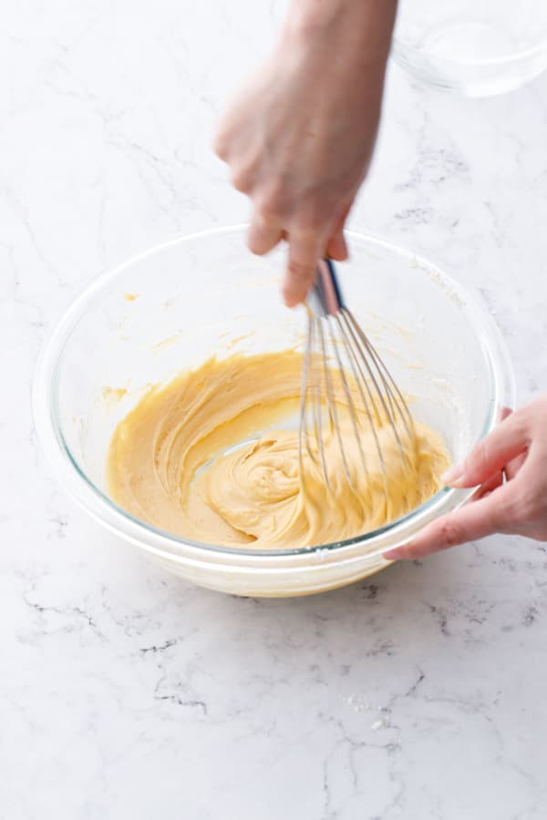 Whisking feuilletine batter in a glass mixing bowl until smooth and uniform.